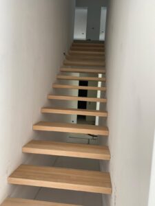 Dębowe schody półkowe wkuwane w ścianę. Wykończenie olejowosk w kolorze naturalnego drewna.